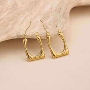 Macro detail of gold U-shaped earrings with spiral hammer texture and latch-back closure