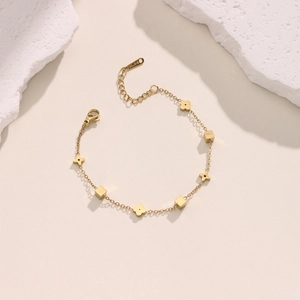 Detailed close-up of 18K gold-plated star and flower charms on a fine link chain bracelet