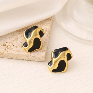 Irregular wave-shaped gold earrings with black enamel finish on a stone pedestal