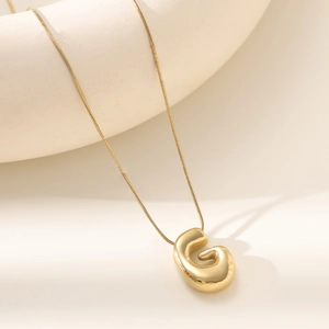 Detailed view of polished 18K gold letter G pendant on snake chain with warm background