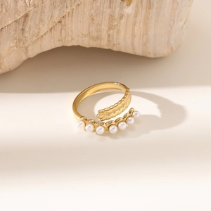 Detaillierte Makroansicht des goldenen Bypass-Rings mit Federstruktur und eleganten Perlen