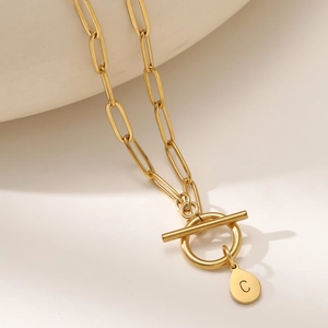 Golden paperclip chain necklace with initial C pendant and toggle clasp on ceramic background