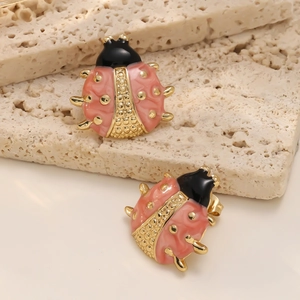 Dettaglio macro di orecchini a coccinella in smalto rosa su sfondo di pietra naturale