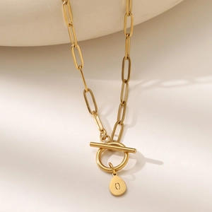Close-up of golden paperclip chain necklace with OT toggle clasp and letter O pendant
