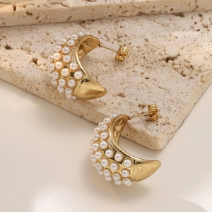 Elegant C-shaped 18K gold plated earrings with white pearls on a travertine stone