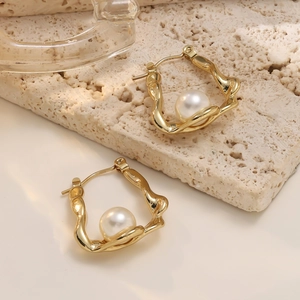 Detail of irregular golden bow earrings with pearls on a natural stone surface