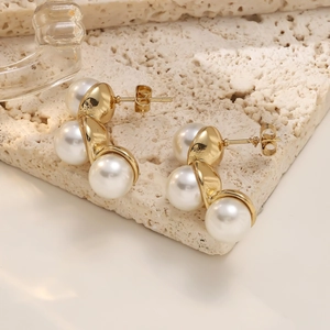 Detail of elegant triple pearl stud earrings with gold setting on a beige stone surface