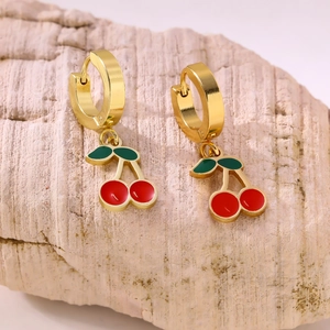 Detail of red cherry pendant earrings with golden hoops on a textured stone surface