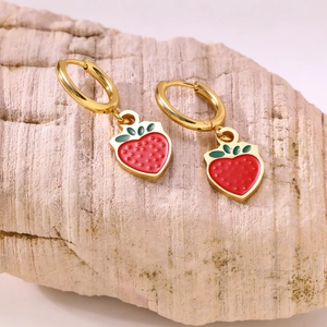 Creative gold fruit hoop earrings with red strawberry charms on pink stone background