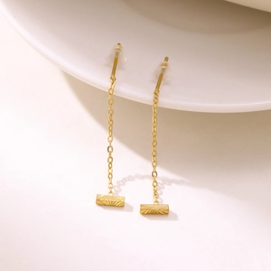 Macro shot of long gold chain earrings with engraved rectangular sunburst pendants