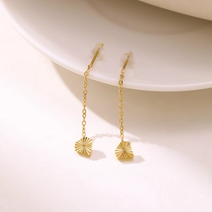 Detail shot of long gold tassel earrings with textured heart charms on white ceramic