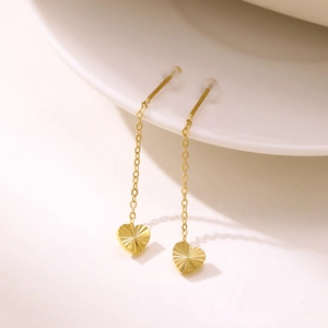 Elegant gold tassel earrings with textured heart pendants hanging on a white ceramic rim