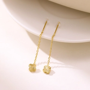 Detailed macro view of gold tassel earrings with clover charms and delicate link chains