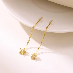 Detailed view of gold star tassel earrings with sunburst texture on a white ceramic edge