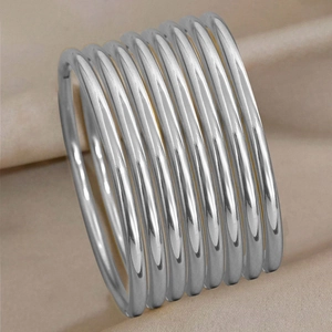 Polished silver 3mm stainless steel bangles layered on champagne silk background