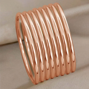Detail of 3mm rose gold titanium steel bangles stacked on soft fabric background
