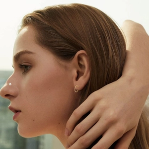 Close-up of golden minimalist hoop earring and small nose stud on model in natural light
