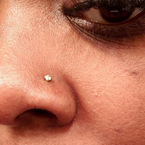 Minimalist gold nose stud with round cubic zirconia crystal on human skin close-up