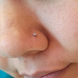 Close-up of a silver stainless steel nose stud with a clear four-prong set cubic zirconia