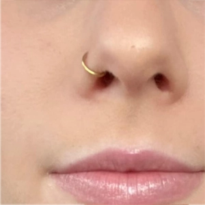 Close-up of a slim gold stainless steel nose ring hoop worn on a female nostril