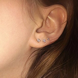 Close-up of three graduated silver cubic zirconia stud earrings worn on an ear