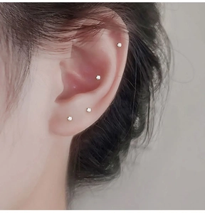 Close-up of four-claw stainless steel nose studs with clear zircons on model ear