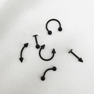 Dettaglio di 6 piercing neri in acciaio inossidabile con punte a sfera e coniche su tessuto