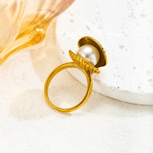 Eleganter goldener Muschelring mit glänzender weißer Perle auf einem weißen Steinsockel