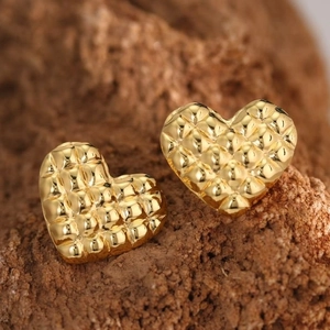 Detailed macro view of gold heart stud earrings featuring a textured quilted pattern