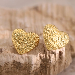 Macro shot of gold heart studs with textured hammered finish on a natural stone base