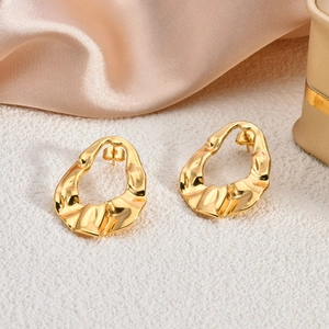 Macro detail of gold-plated irregular lava textured oval stud earrings on white surface