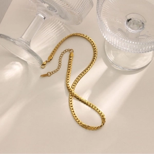 Golden flat Cuban link chain necklace displayed elegantly with glass decor on a neutral base