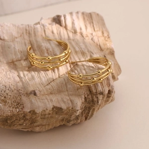 Close-up of triple-layered 18k gold plated stainless steel C-shaped earrings on stone