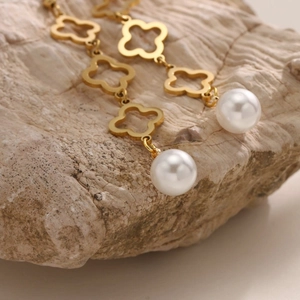 Détail de boucles d'oreilles longues trèfle doré avec perles blanches sur fond de pierre