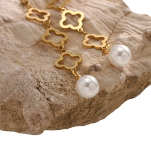 Boucles d'oreilles trèfle dorées avec pendentifs perles sur fond de pierre texturé