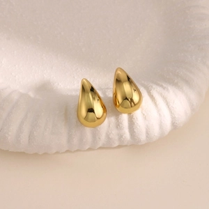 Vista macro de pendientes de gota dorados con acabado de espejo pulido en un plato blanco