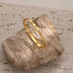 Detail of gold honeycomb bangle with sparkling zircons set against a natural stone background