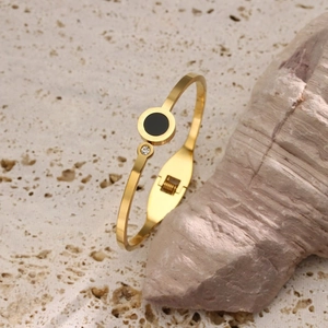 Detailed close-up of gold-plated bangle with black disc and zircon on textured stone