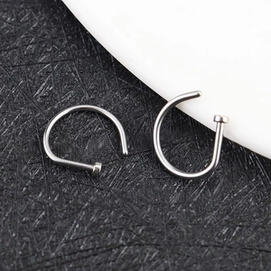 Macro shot of two silver stainless steel C-shaped nose rings on a textured background