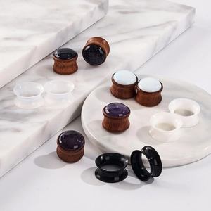 Close-up of wood and silicone ear gauges set featuring natural stone inlays on marble base