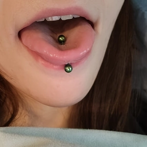 Detail shot of a dark green stainless steel tongue piercing barbell worn on the tongue