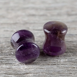 Macro shot of polished purple amethyst stone ear plugs on a textured wooden background