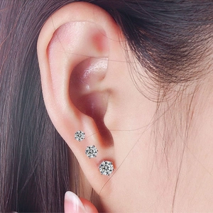 Close-up of three 6-claw cubic zirconia stud earrings in varying sizes on a model's ear