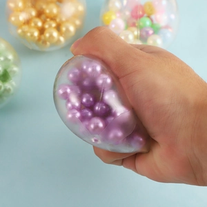 Hand squeezing a purple stress relief ball filled with soft beads on blue background
