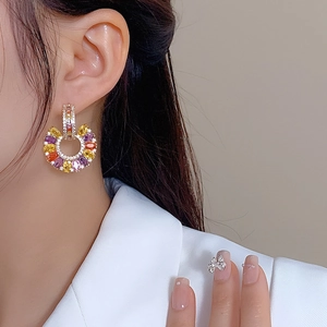 Close-up of C-shaped drop earrings with colorful gemstones and zirconia on a model