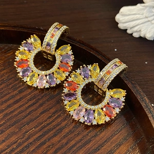 Close-up of golden C-shaped earrings with colorful marquise-cut zircons and micro-pave crystals
