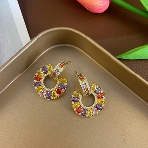 Close-up of gold C-shaped earrings with colorful pave-set oval gemstones on a tray