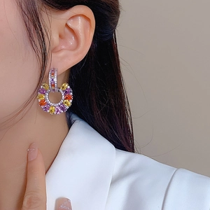 Close-up of C-shaped drop earrings with colorful zircon stones worn by a model