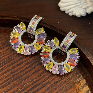 Macro view of C-shaped drop earrings featuring colorful oval zircons on a dark wood tray