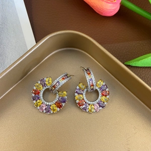 Detail of C-shaped drop earrings with colorful gemstones and pavé zircon on golden tray